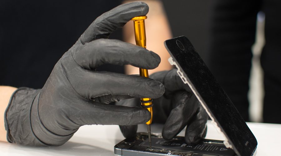 Riparazione di un dispositivo elettronico con cacciavite, guanti neri in primo piano.