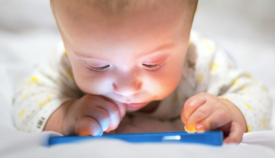 **Alt text (Italiano):** Bambino affascinato dalla tecnologia mentre guarda uno smartphone acceso.